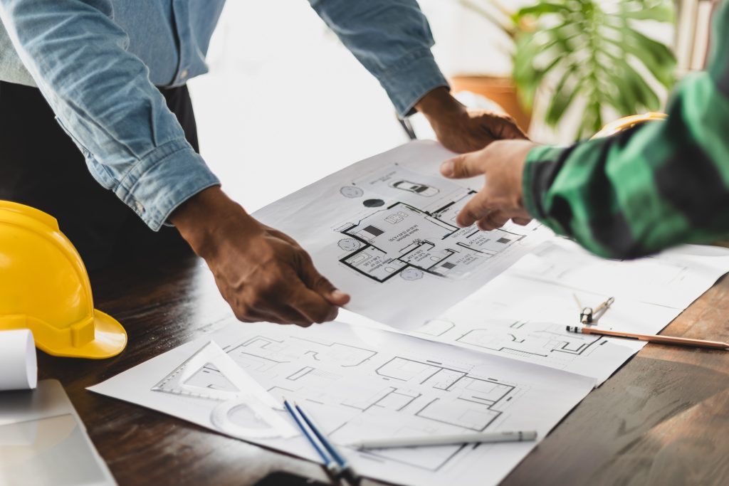 Two people are collaborating and examining architectural blueprints on a wooden desk